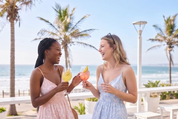 Two friends with Tjello spritzes at a beachfront table